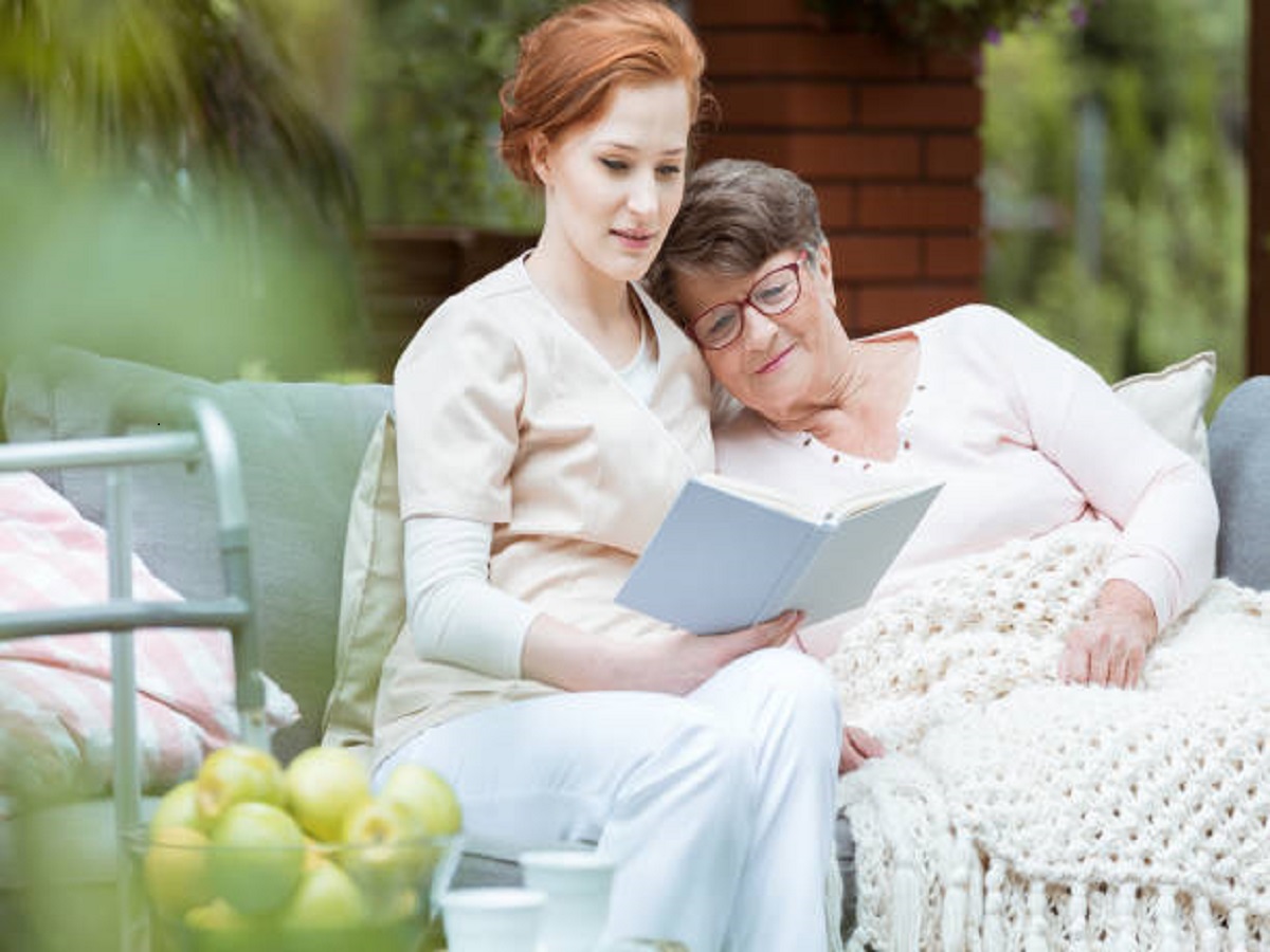 Elder lady in glasses covered with blanket resting her head on nurse's shoulder