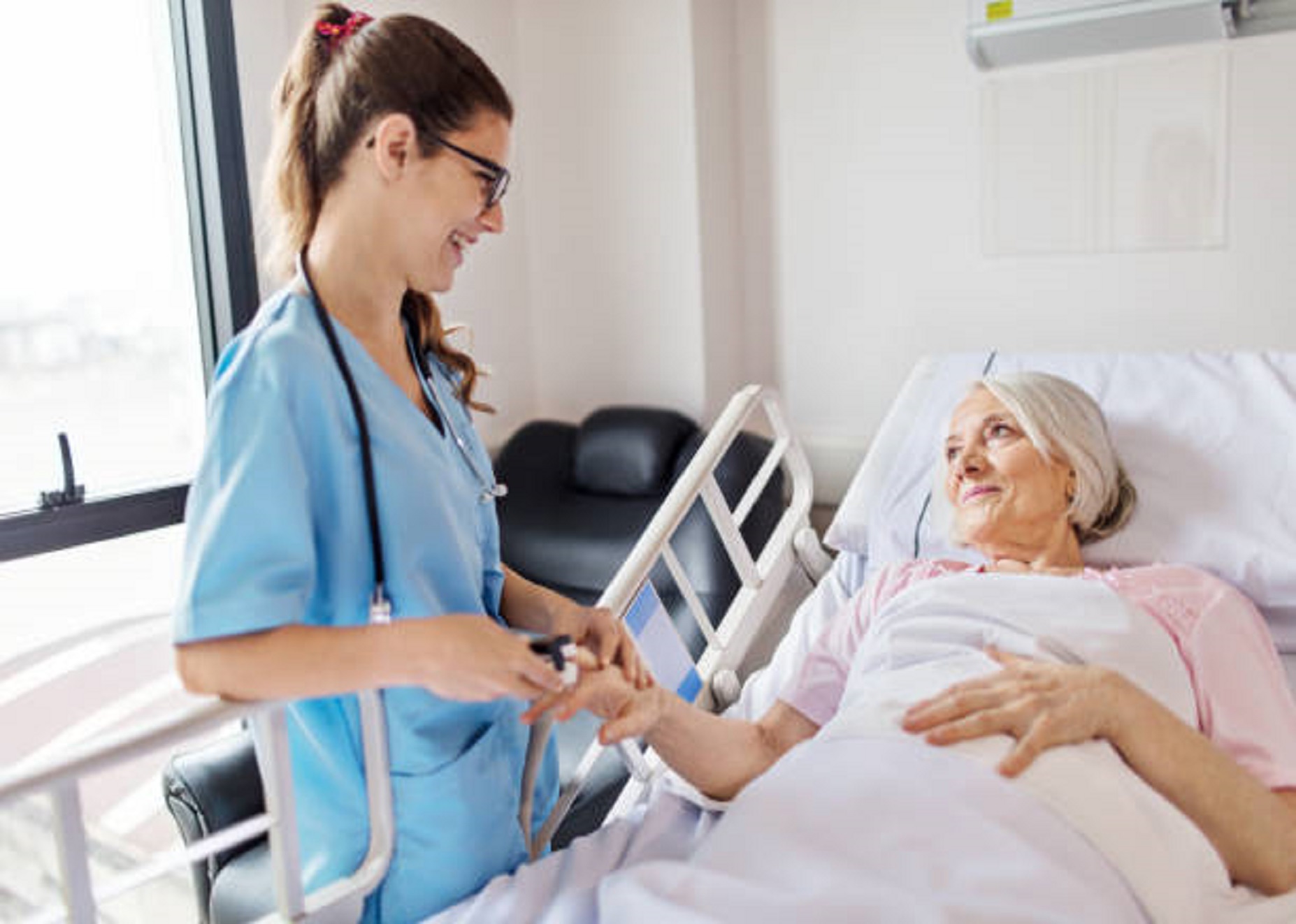 Female nurse adjusting pulse oxymeter on senior woman's finger. Young professional is smiling while looking at patient. Medical worker is examining elderly woman lying on hospital bed.